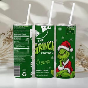 Pode incluir: Três copos cilíndricos com palhinhas brancas, com um design verde inspirado no Grinch. Os copos apresentam informações nutricionais, o texto The Grinch Edition, Green Apple e uma ilustração da personagem com um gorro de Pai Natal.