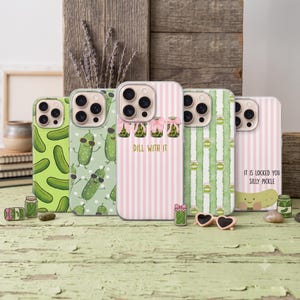 May include: Five smartphone cases featuring pickle-themed designs. One case has a green pickle pattern, another shows dancing pickles with sunglasses, one has pink stripes with jars and the text DILL WITH IT, one has green stripes, and one has a pickle with the text IT IS LOCKED YOU SILLY PICKLE.