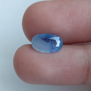 Könnte beinhalten: Ein ovaler, facettierter hellblauer Edelstein mit sichtbaren inneren Einschlüssen und einem durchscheinenden Aussehen. Der Stein hat eine polierte Oberfläche mit mehreren geometrischen Facetten, die das Licht reflektieren und eine sanfte, himmelblaue Farbe zeigen.