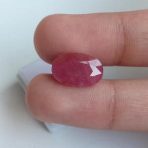 Może przedstawiać: Owalny, fasetowany kamień szlachetny o głębokim różowo-czerwonym odcieniu. Kamień posiada polerowaną powierzchnię z wieloma trójkątnymi fasetami, które odbijają światło, ukazując półprzezroczystą strukturę oraz żywy, nasycony kolor w całym klejnocie.