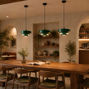 Puede incluir: Tres lámparas colgantes escalonadas con un acabado verde oscuro brillante y detalles interiores en tono dorado, suspendidas del techo por cables negros delgados sobre una mesa de comedor de madera larga con sillas de madera a juego.