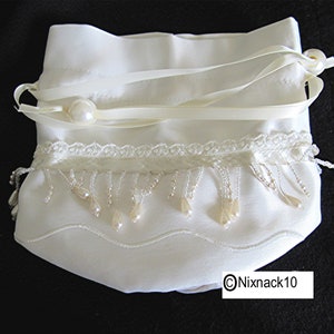 May include: A white satin drawstring bag with a pearl trim and a white satin ribbon. The bag has a beaded fringe and a pearl accent.
