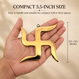Może przedstawiać: Złoty metalowy ornament w kształcie symbolu swastyki o gładkiej, odblaskowej powierzchni z małym okrągłym oczkiem u góry do zawieszenia. Obiekt ma wymiary 14 cm na 14 cm, co zostało zaznaczone w tekście oraz na graficznej skali na obrazie.