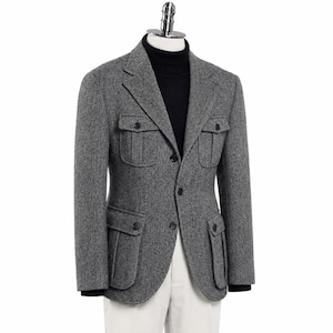May include: A grey herringbone blazer featuring a notched lapel, three dark buttons, and four large patch pockets with buttoned flaps. The blazer is layered over a black turtleneck sweater and paired with light-colored trousers on a mannequin.