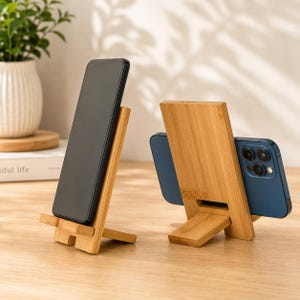 May include: Two light brown bamboo phone stands. One stand holds a black smartphone in a vertical position, while the other stand holds a blue smartphone in a horizontal position, displaying the rear camera lenses on the right side of the device.