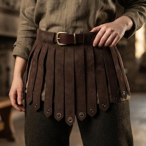 May include: A dark brown leather belt featuring a series of vertical hanging strips that form a skirt-like layer. The belt is secured at the waist with a simple brass-toned metal buckle, and each individual leather strip is finished with a small metal stud.