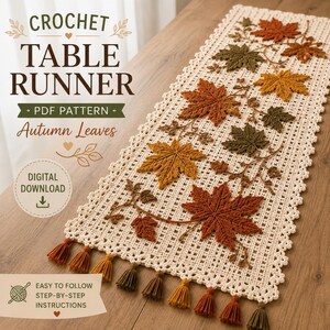 Pode incluir: Um caminho de mesa de crochê na cor creme com um padrão de grade intrincado e uma borda decorativa. O caminho é adornado com folhas de outono tridimensionais em tons de ferrugem, laranja e verde-oliva, finalizado com pequenas borlas nas pontas.