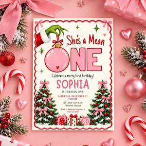 May include: A rectangular birthday invitation card featuring a green furry hand holding a pink Christmas ornament. The text reads: She's a Mean ONE, Celebrate a merry first birthday! SOPHIA IS TURNING ONE, SATURDAY, DECEMBER 12, 2:00 PM, 123 Candy Cane Lane, Portland, Oregon, RSVP to Emma by December 1 (555) 123-4567.