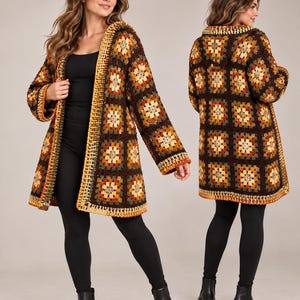 Puede incluir: Un cárdigan de ganchillo de manga larga con capucha, que presenta un patrón repetitivo de cuadrados granny en tonos marrón oscuro, naranja, amarillo y verde oliva. La prenda tiene una base marrón oscuro, capucha y un borde acabado.