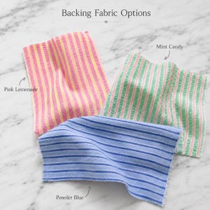 Może przedstawiać: Trzy pr&oacute;bki tkanin z nagł&oacute;wkiem Backing Fabric Options. Jedna pr&oacute;bka ma r&oacute;żowo-ż&oacute;łte pionowe paski z etykietą Pink Lemonade. Druga ma zielono-r&oacute;żowe pionowe paski z etykietą Mint Candy. Trzecia ma niebiesko-białe poziome paski z etykietą Powder Blue.