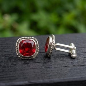 Puede incluir: Un par de gemelos de plata con una piedra preciosa de color rojo intenso, tallada en forma cuadrada y engastada en un borde de estilo cuerda trenzada. Los gemelos tienen un acabado en plata pulida y un mecanismo de cierre estándar.
