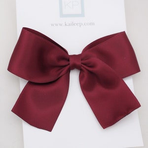 May include: A large, burgundy satin bow. The bow is displayed on a white card with the text "WINE" printed on it.