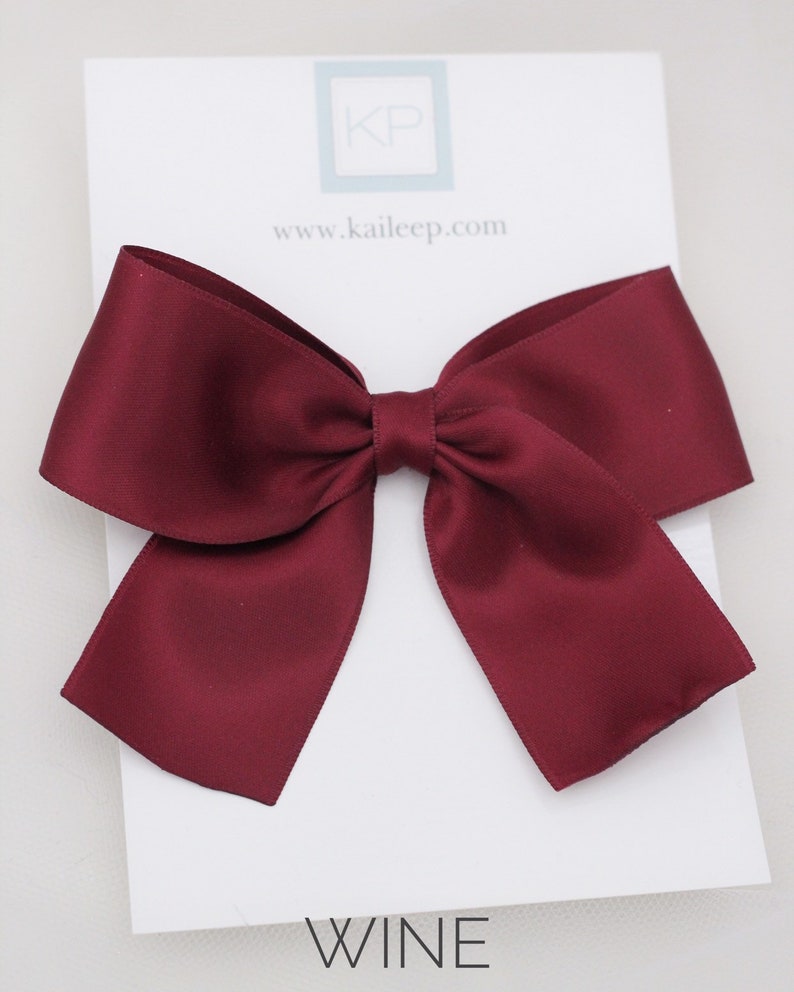 May include: A large, burgundy satin bow. The bow is displayed on a white card with the text "WINE" printed on it.