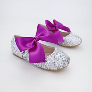 May include: A pair of silver glitter ballet flats with a large purple satin bow on each shoe.