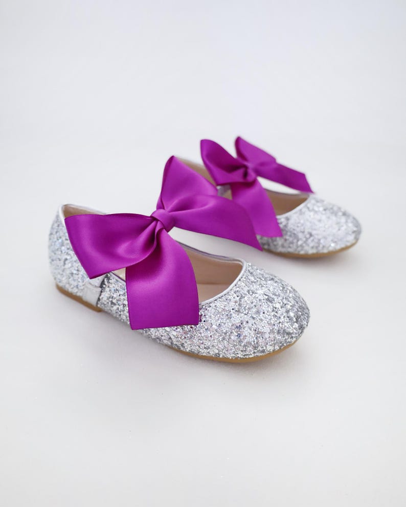 May include: A pair of silver glitter ballet flats with a large purple satin bow on each shoe.