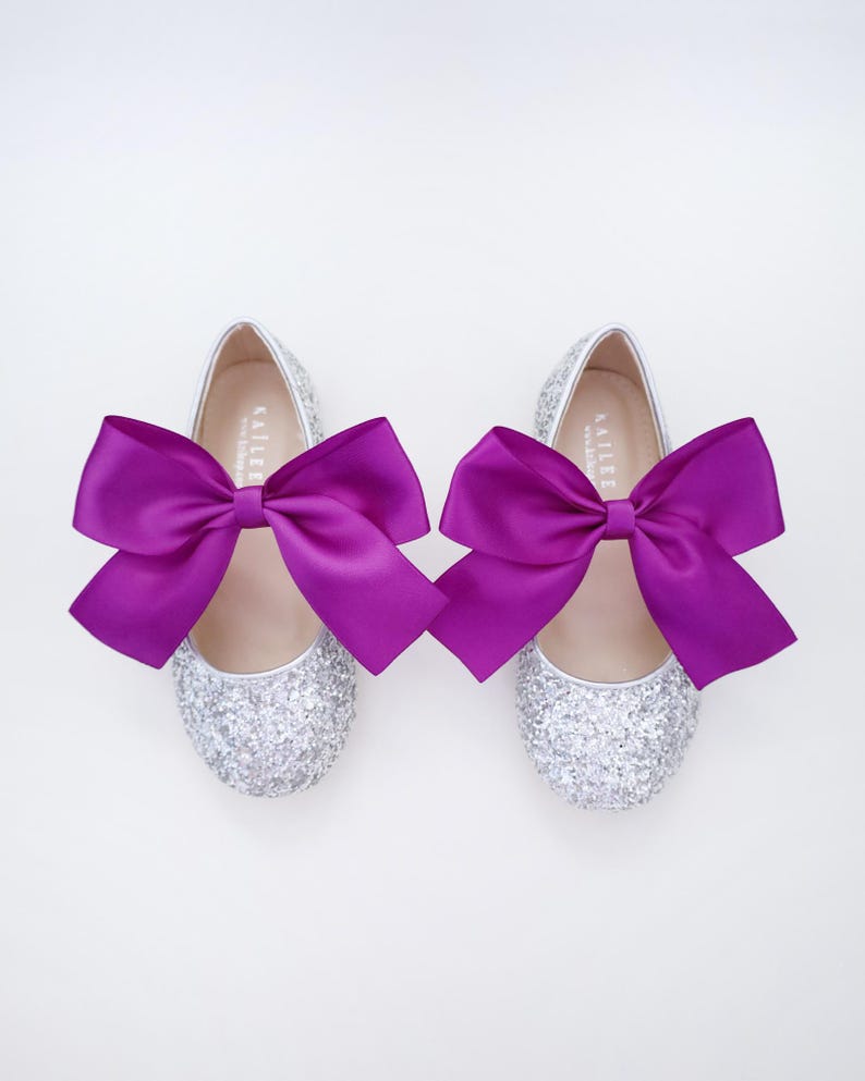 May include: A pair of silver glitter ballet flats with purple satin bows. The shoes have the word "Kailee" written on the inside.