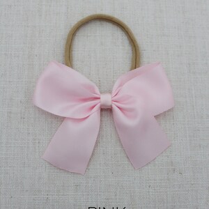 May include: A pink satin bow tied on a nude elastic headband. The headband is for babies and toddlers.