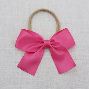May include: A fuchsia satin bow hair tie with a nude elastic band.