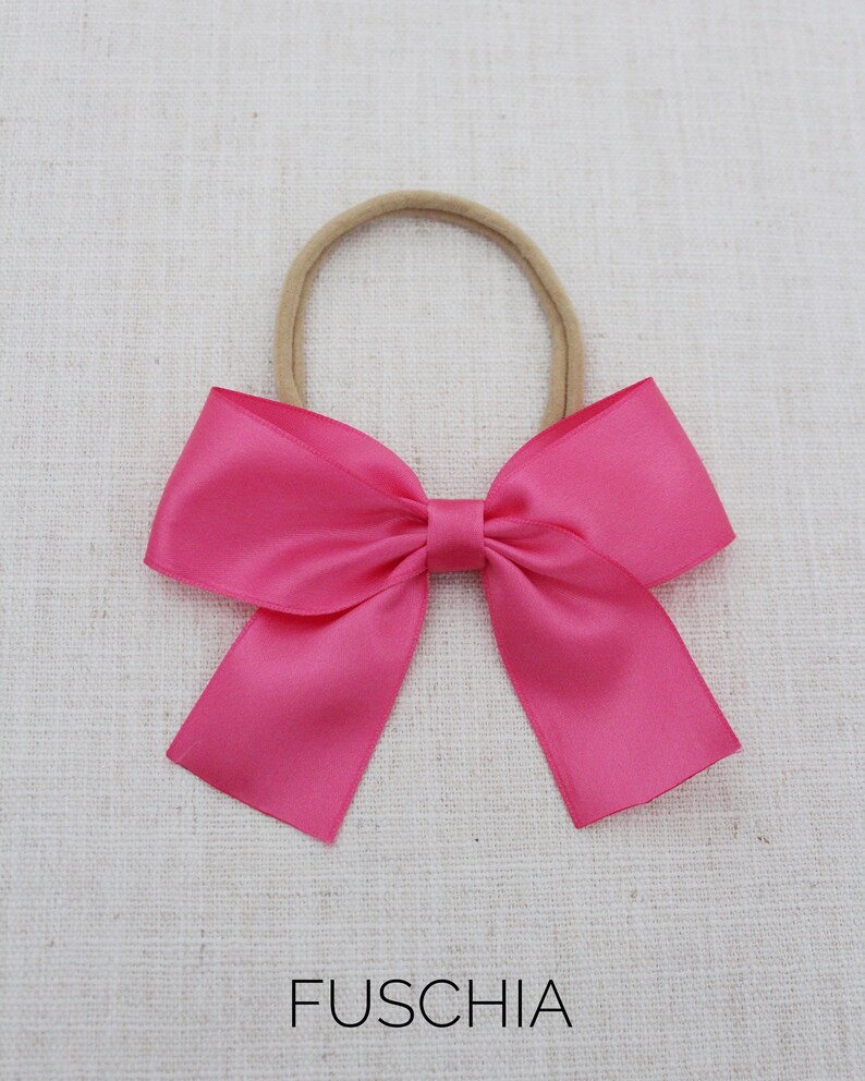 May include: A fuchsia satin bow hair tie with a nude elastic band.