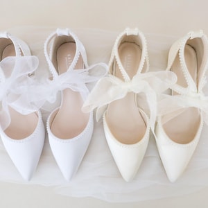 May include: Two pairs of white satin bridal shoes with pearl trim and delicate white ribbon bows.