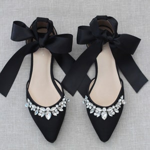 May include: Black satin bridal flats with a pointed toe and a crystal embellishment on the front. The shoes have long black satin ribbons that tie at the ankle.