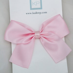 May include: A large pink satin bow with a small centre loop. The bow is on a white card with the text "KP" and "www.kaileep.com" printed on it. The word "PINK" is printed at the bottom of the card.