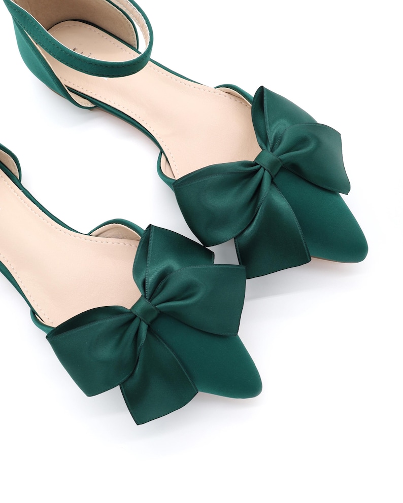 May include: A pair of emerald green satin flats with a pointed toe and a large bow on the top of each shoe.