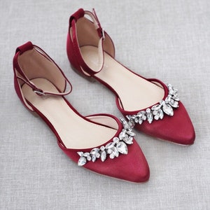Puede incluir: Un par de zapatos planos de sat&eacute;n burdeos con punta. Los zapatos tienen una correa en el tobillo y est&aacute;n adornados con cristales transparentes brillantes en la punta. Dise&ntilde;ados para ocasiones especiales.