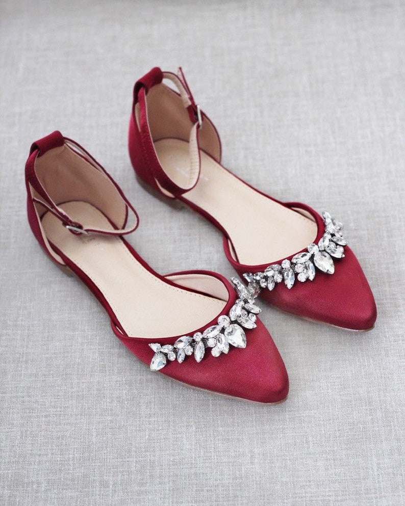 Puede incluir: Un par de zapatos planos de sat&eacute;n burdeos con punta. Los zapatos tienen una correa en el tobillo y est&aacute;n adornados con cristales transparentes brillantes en la punta. Dise&ntilde;ados para ocasiones especiales.