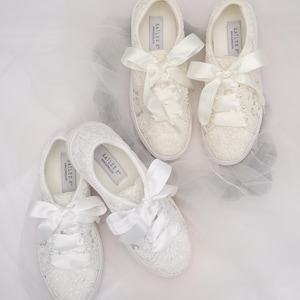 May include: Four pairs of white lace sneakers with satin ribbon laces. The sneakers have a low profile and a white sole. The brand name "KAILEE F" is printed on the inside of the shoe. The shoes are arranged on a white surface.