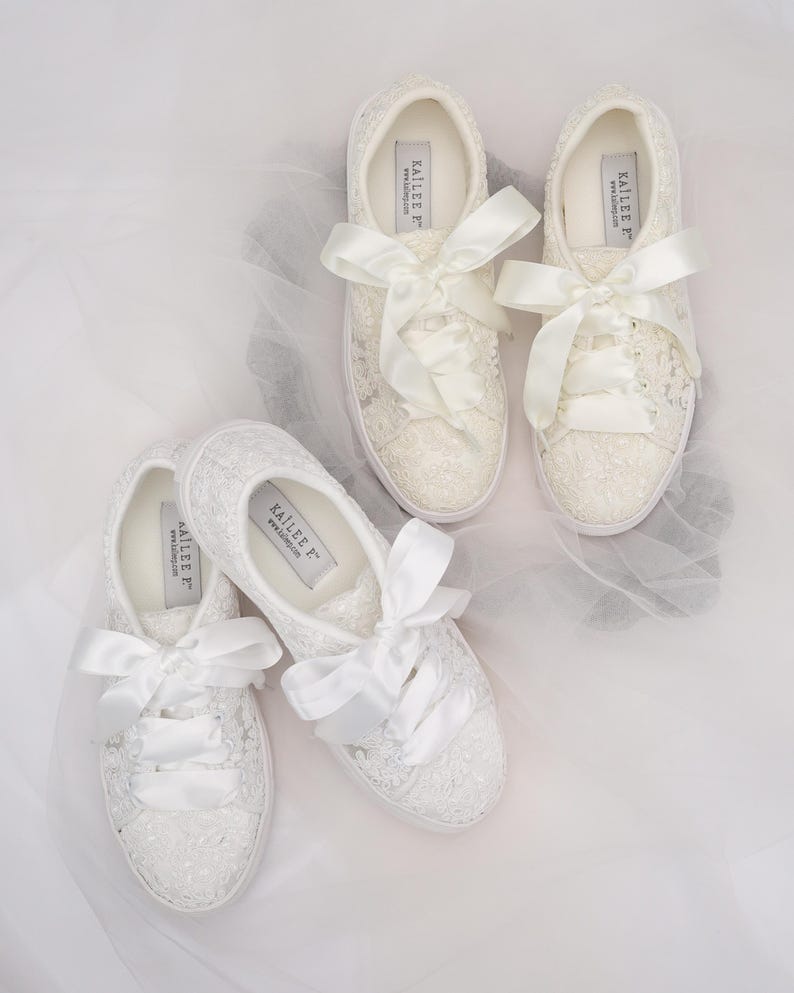 May include: Four pairs of white lace sneakers with satin ribbon laces. The sneakers have a low profile and a white sole. The brand name "KAILEE F" is printed on the inside of the shoe. The shoes are arranged on a white surface.