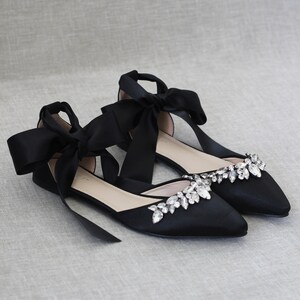 May include: Black satin flats with a pointed toe and a large crystal embellishment on the vamp. The shoes have a ribbon tie that wraps around the ankle.