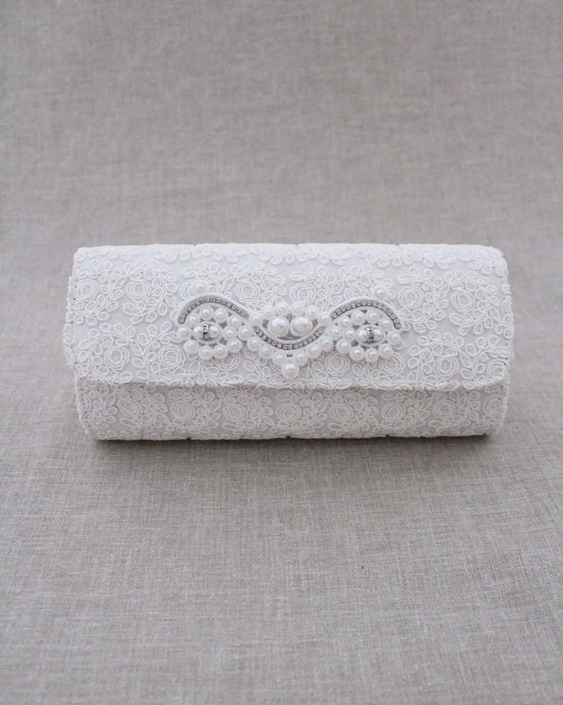 May include: White lace clutch with a pearl and rhinestone embellishment.