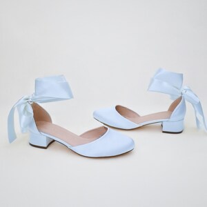 May include: A pair of light blue satin heeled shoes with a bow on the ankle strap.