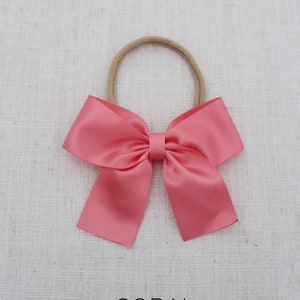 May include: A coral satin hair bow with a nude elastic headband.