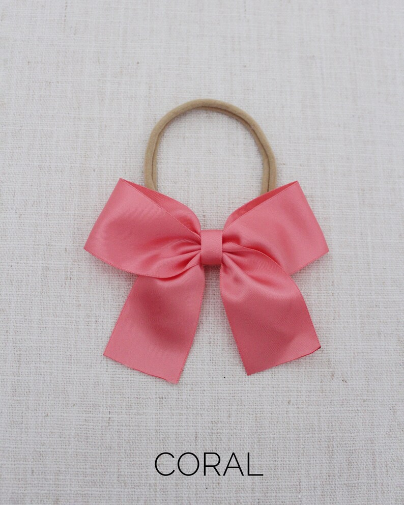 May include: A coral satin hair bow with a nude elastic headband.