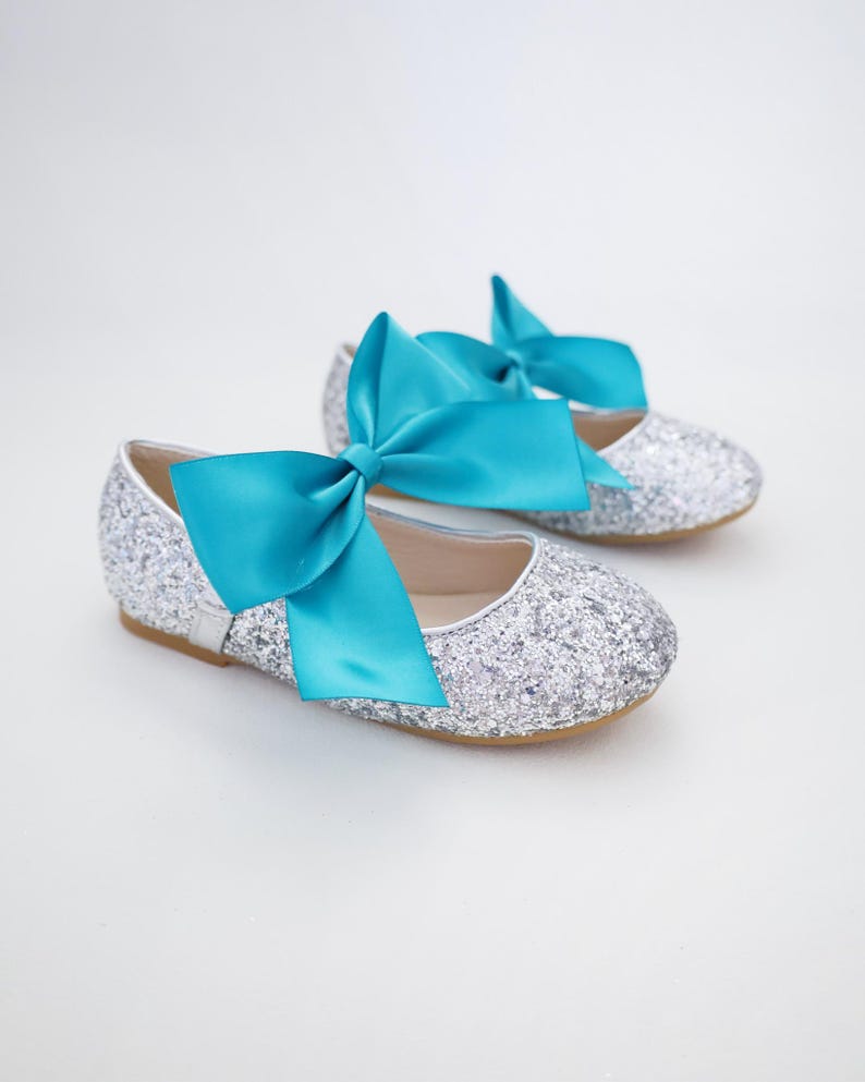 May include: Silver glitter ballet flats with a large turquoise satin bow. The shoes are for a child.
