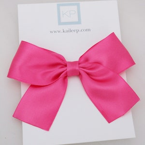 May include: A large fuchsia satin bow with a white card that says "KP" and "www.kaileep.com" and the word "FUCSIA" at the bottom.