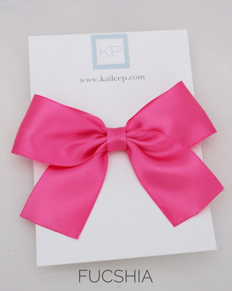 May include: A large fuchsia satin bow with a white card that says "KP" and "www.kaileep.com" and the word "FUCSIA" at the bottom.