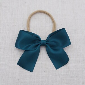 Puede incluir: Un lazo de sat&eacute;n azul oscuro atado con una diadema el&aacute;stica de color carne.  DARK TEAL.