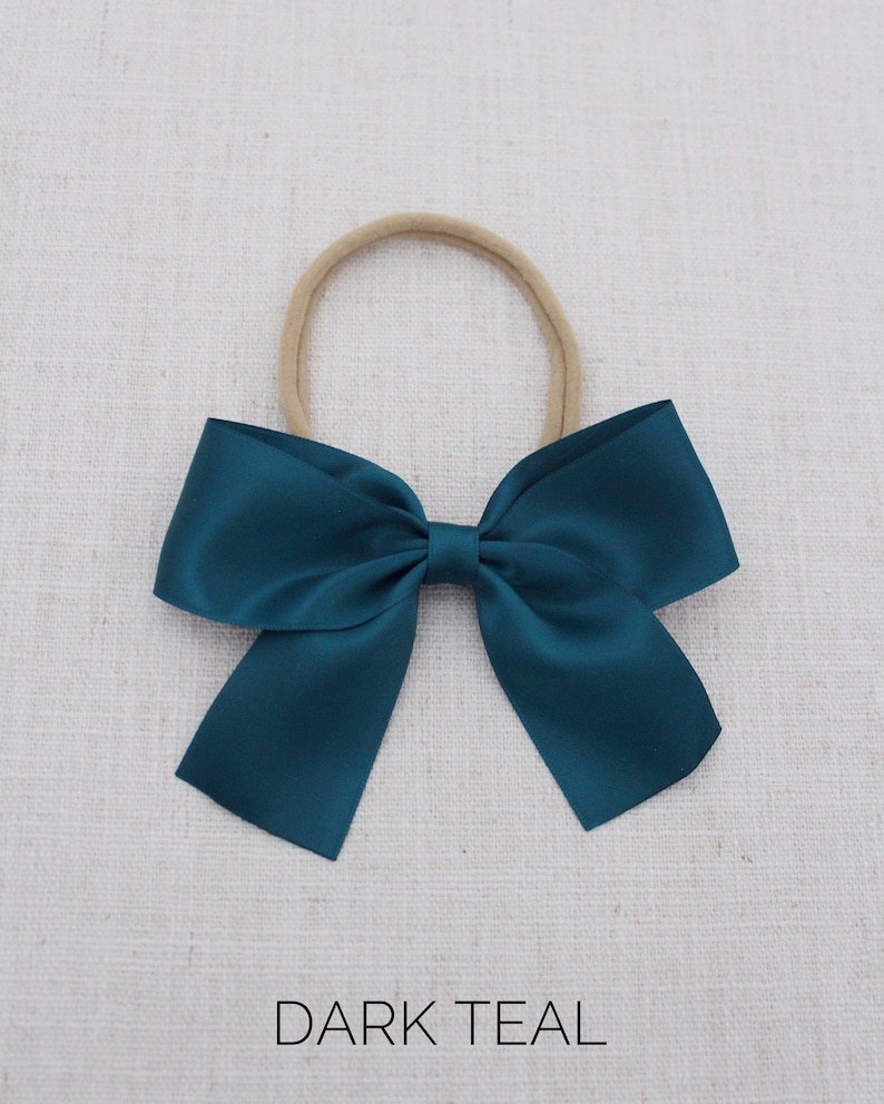 Puede incluir: Un lazo de sat&eacute;n azul oscuro atado con una diadema el&aacute;stica de color carne.  DARK TEAL.