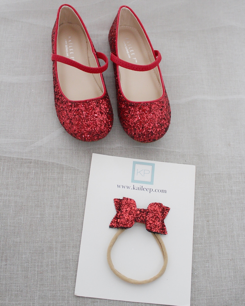 Puede incluir: Zapatos rojos de purpurina con una diadema de lazo rojo. Los zapatos tienen una correa en la parte superior y la diadema es de el&aacute;stico. Los zapatos y la diadema est&aacute;n decorados con purpurina roja. La diadema tiene el texto "KP" y "www.kaileep.com" impreso en ella.