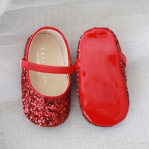 Puede incluir: Un par de zapatos de beb&eacute; de brillo rojo con una suela de charol rojo brillante. Los zapatos tienen una correa en la parte superior y las palabras "KAILI  P.M." est&aacute;n impresas en el interior del zapato.
