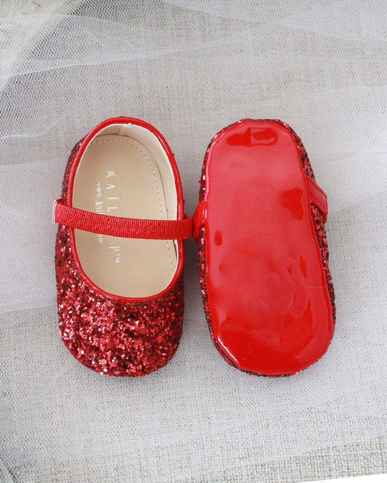 Puede incluir: Un par de zapatos de beb&eacute; de brillo rojo con una suela de charol rojo brillante. Los zapatos tienen una correa en la parte superior y las palabras "KAILI  P.M." est&aacute;n impresas en el interior del zapato.