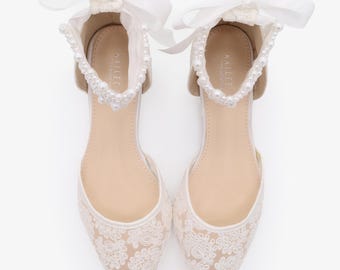 May include: Ivory lace flats with pointed toes. The shoes have a delicate floral lace pattern and are embellished with a pearl-lined ankle strap and a white satin bow. These shoes are suitable for special occasions, such as weddings.