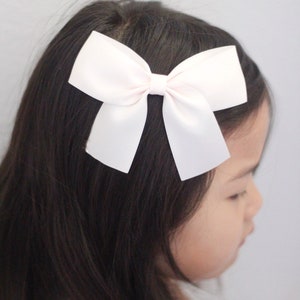 May include: A white satin bow hair clip. The bow is tied in a classic shape with two loops and a centre knot.