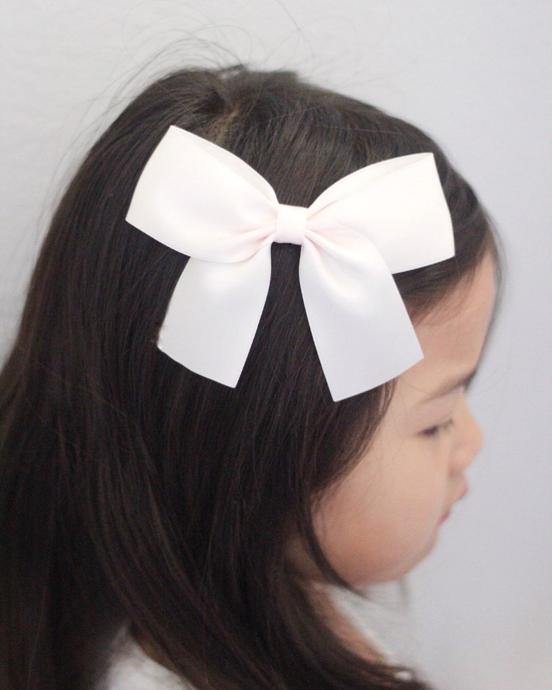 May include: A white satin bow hair clip. The bow is tied in a classic shape with two loops and a centre knot.