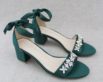 May include: A pair of emerald green satin heeled sandals with a low block heel and a crystal embellishment on the strap. The sandals have a ribbon tie closure at the ankle.