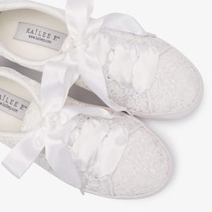 May include: White lace sneakers with satin ribbon laces. The sneakers feature a delicate floral lace pattern and a white rubber sole. The brand name "KAILEE P." is visible on the inner sole.