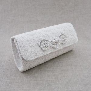 May include: White lace clutch with a pearl and rhinestone embellishment.